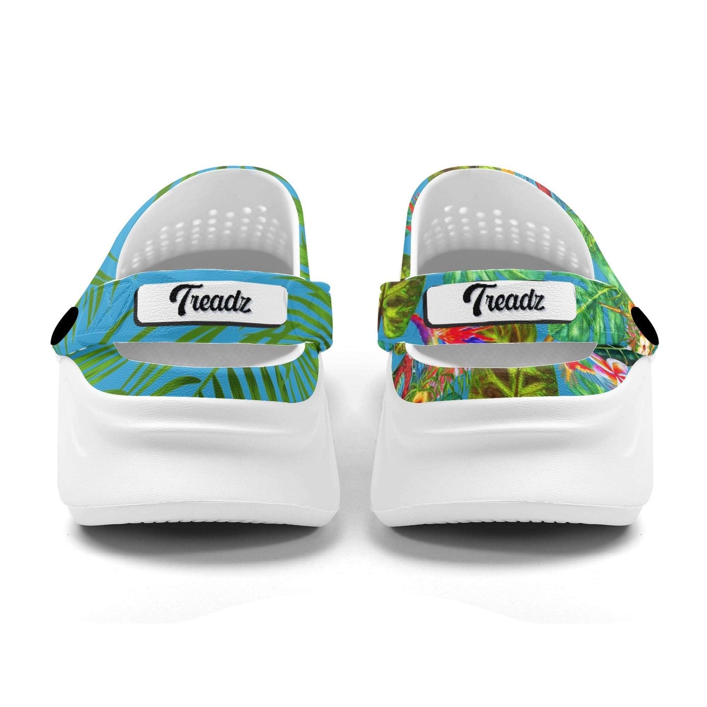 Treadz Mismatch Clogs Tropicana featuring white EVA clog design with mismatched tropical patterns - left clog with blue and green palm leaves, right clog with vibrant tropical foliage and birds, both with white soles and Treadz branded straps