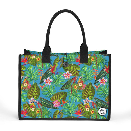 The Mismatch Tote Bag - Tropicana features vibrant tropical pattern with lush green palm leaves, pink flowers, and colorful birds on turquoise background, black handles and trim, and secure button closure for stylish everyday use