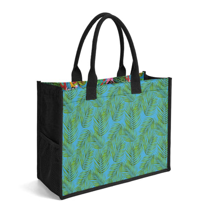 The Mismatch Tote Bag Tropicana featuring a vibrant tropical design with green palm leaves pattern on turquoise background, black canvas handles and sides, spacious rectangular shape with sturdy construction