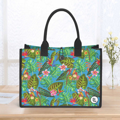 The Mismatch Tote Bag - Tropicana featuring vibrant tropical pattern with green palm leaves, exotic flowers, and parrots on turquoise background, with black handles and secure button closure, perfect for everyday use