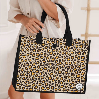 The Mismatch Tote Bag - Safari shown held against cream background, featuring bold leopard print pattern with black trim handles and button closure, perfect for everyday use and shopping trips