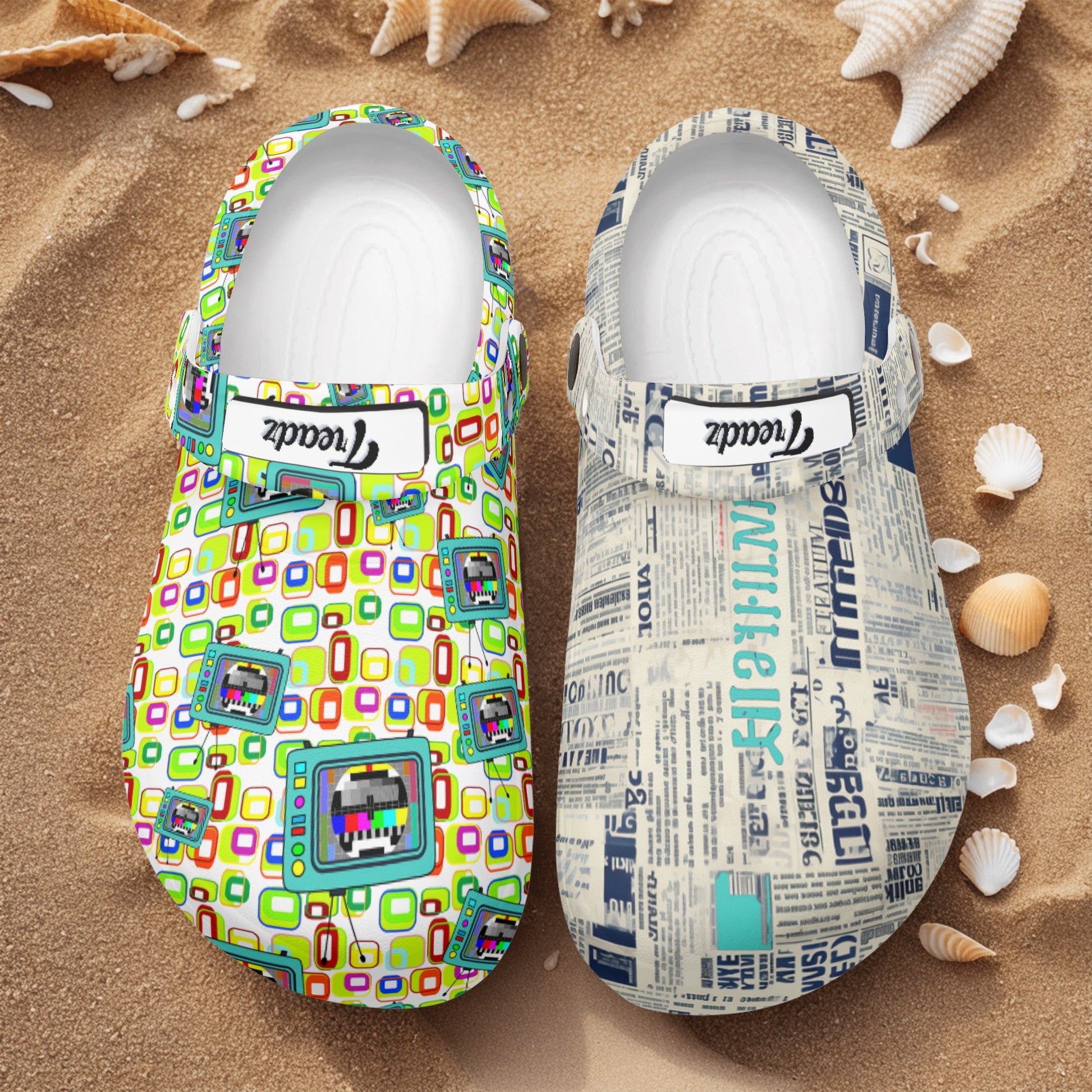 Treadz Nursing Slide On Mismatch Clogs - Retro Media shown on sandy beach with seashells, featuring mismatched designs - one clog with colorful retro TV pattern, other with vintage newspaper print, both photographed from above on beach sand background