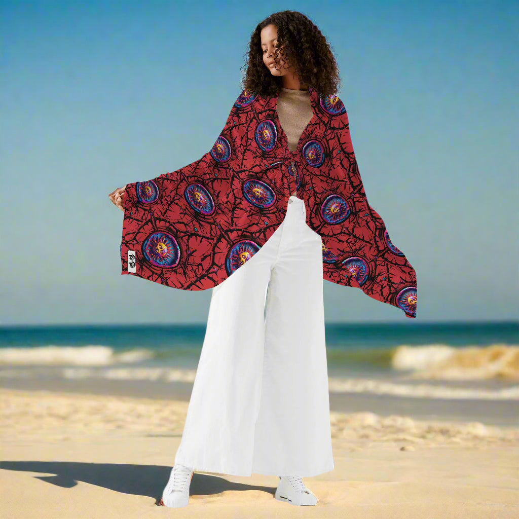 Womens Sarong Luna Anarchy RED displayed as a beach cover-up with vibrant red and blue circular pattern design, shown draped elegantly with arms extended to showcase the full width and flowing fabric texture against white pants