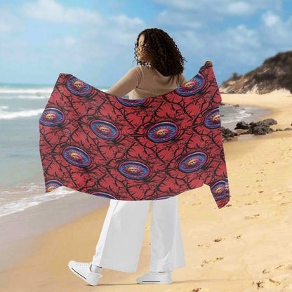 Womens Sarong - Luna Anarchy RED displayed on beach, flowing red fabric with blue circular mandala patterns against ocean backdrop, showcasing versatile beach cover-up with traditional print design on sandy shoreline.