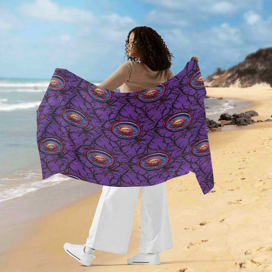 A person on a sandy beach holding up a Luna Anarchy PURPLE sarong featuring vibrant purple fabric with circular medallion patterns, showcasing the flowing material against an ocean backdrop with blue sky and clouds.