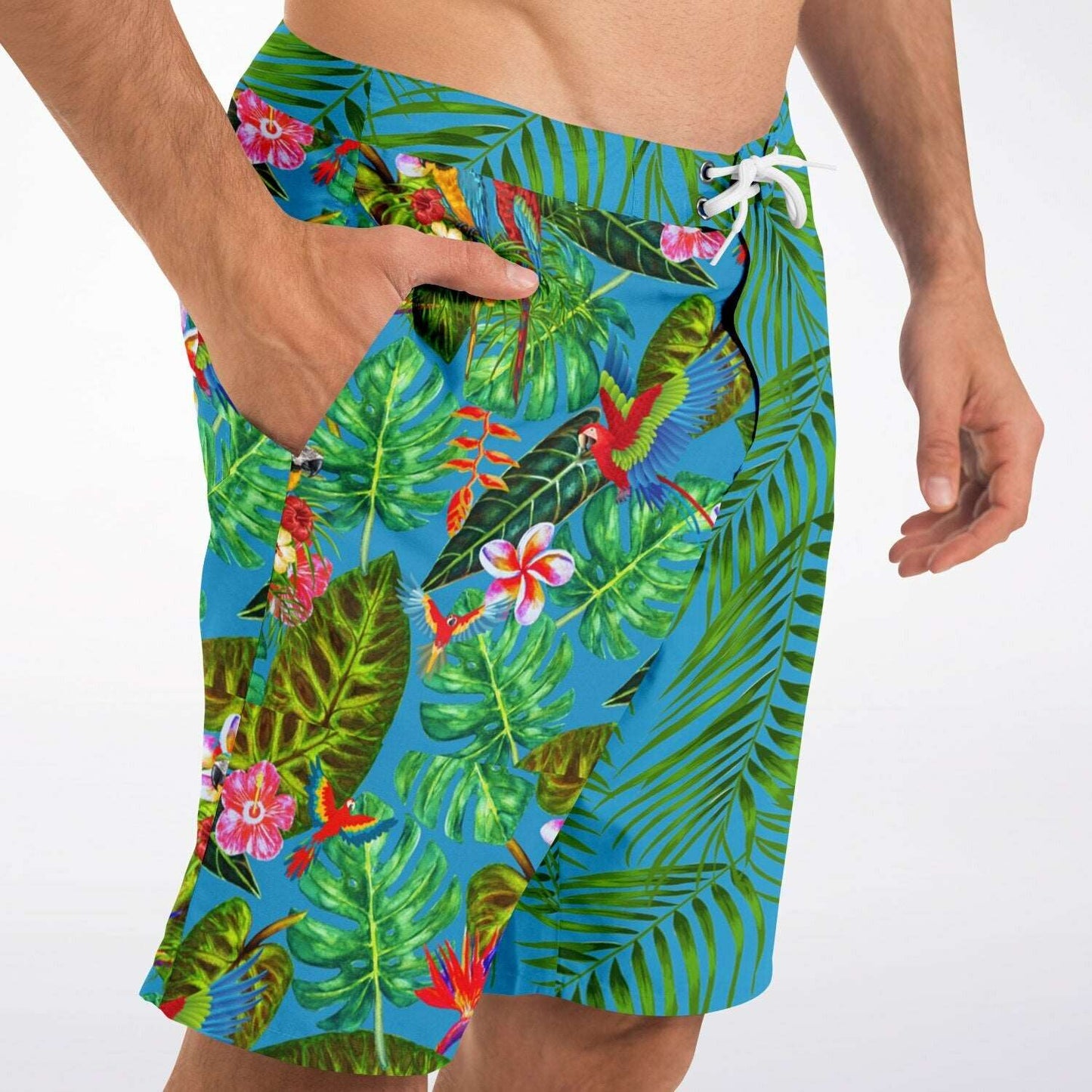 RipTide Men's Mismatch Board Shorts - Tropicana featuring vibrant tropical print with green palm leaves, monstera leaves, colorful flowers, and exotic birds on blue background, with white drawstring and side pockets on casual beachwear