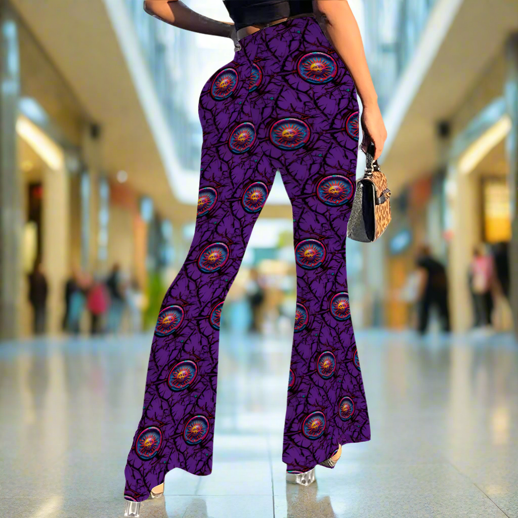 Stretch Bell Bottom Flare - Lunar Anarchy Purple pants shown from waist down, featuring vibrant purple fabric with circular eye-like pattern design, flared leg silhouette, and high-waisted fit. Model wearing stylish pants with handbag accessory, displaying the pants' flattering bell-bottom cut.