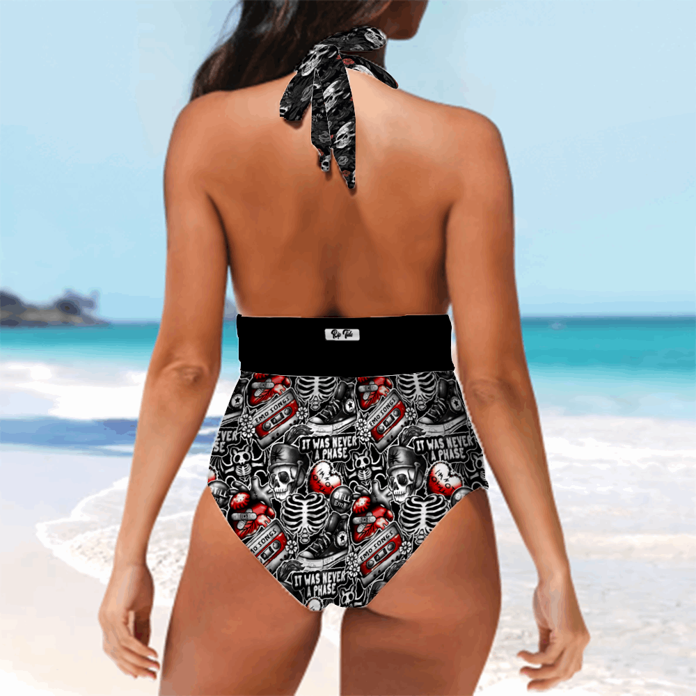 Back view of Rip Tide Tankini One Piece Mismatched Swimsuit featuring a halter neck tie and high-waisted bottom with edgy black, white and red skull pattern design, shown against a tropical beach backdrop with turquoise water