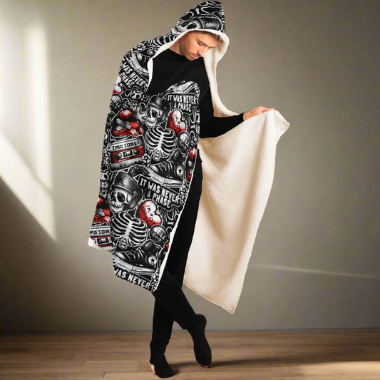 Men's Hooded Blanket - Emo Vibes featuring black and red gothic design with skeletons, cassette tapes, and music-themed artwork on one side and cozy cream fleece on the other. Hooded figure displaying the blanket's reversible design. ShitHot Best Sellers, Men's Hoodie Blankets.