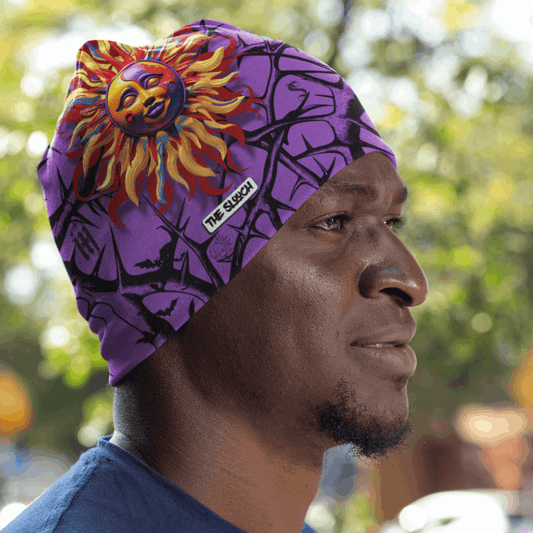 Purple Full Print Pullover Cap - Mismatched Luna featuring vibrant sun design in orange and yellow flames against a deep purple background with abstract tree branch patterns. Polyester beanie style cap with unique artistic print, shown outdoors in natural lighting.