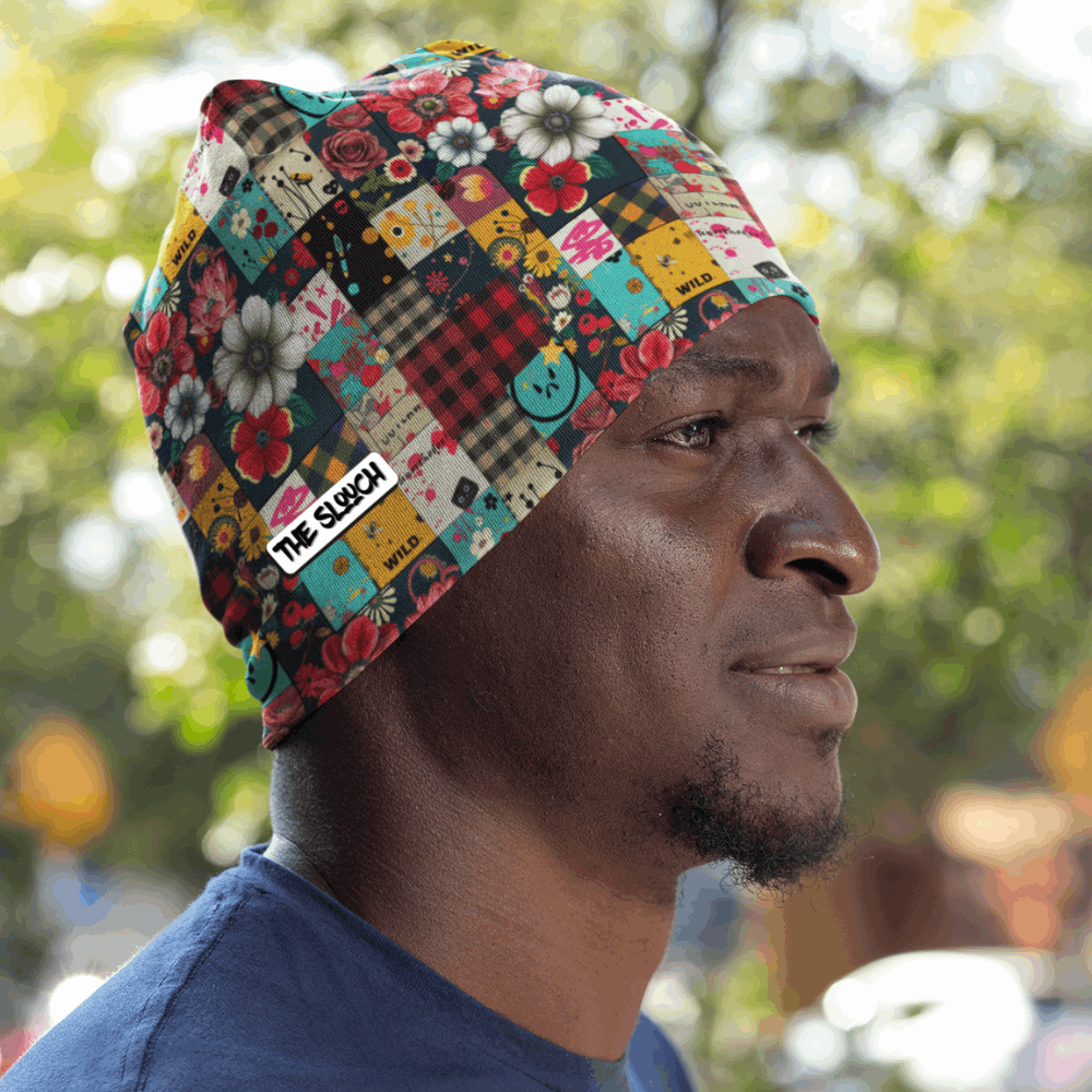 Men's Skull Cap Beanie - Patched Punk shown in profile view featuring a colorful patchwork design with floral patterns, plaid squares, and buttons against a natural outdoor background. The beanie displays vibrant mix of red, teal, yellow, and pink patches worn with a navy blue shirt.