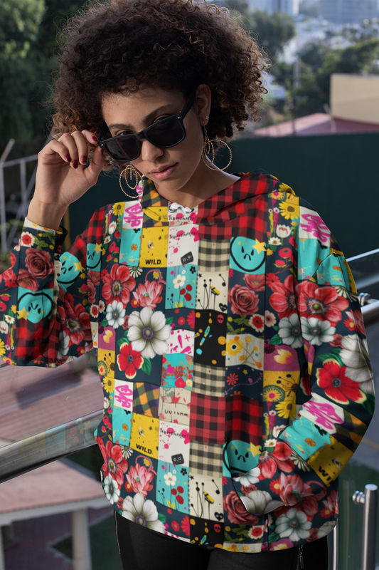 Womens Hoodie - Patched Punk featuring vibrant patchwork design with buffalo plaid, floral prints, and smiley faces in turquoise, red, and yellow. Colorful all-over pattern mixing retro and punk aesthetics, shown outdoors on balcony setting during daytime.