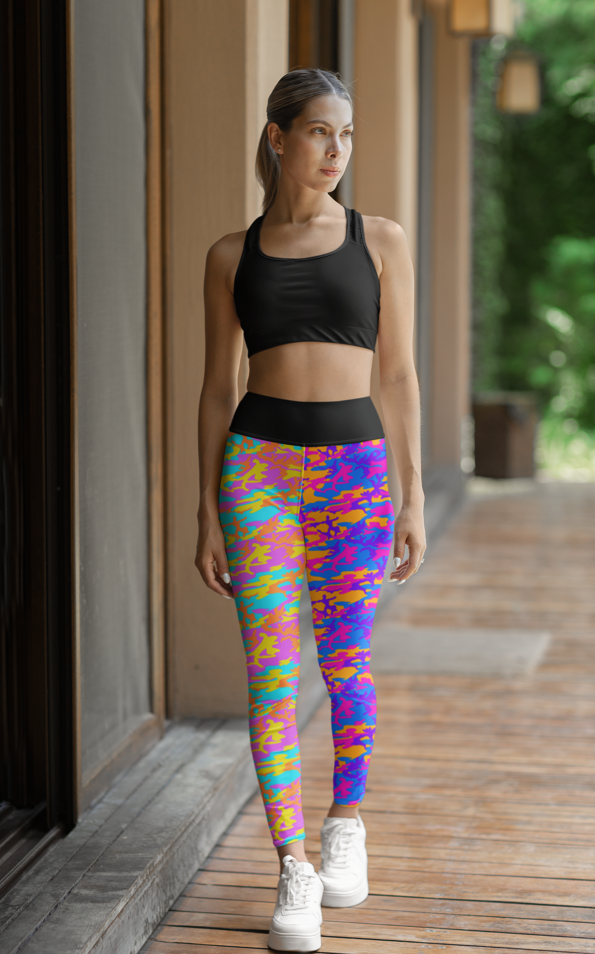 High Waisted Mismatch Core FX Mismatch Leggings in vibrant multicolor camo pattern paired with black sports bra. Athletic wear shown on model in outdoor setting with white sneakers, highlighting the leggings' bold design and high-waisted fit.